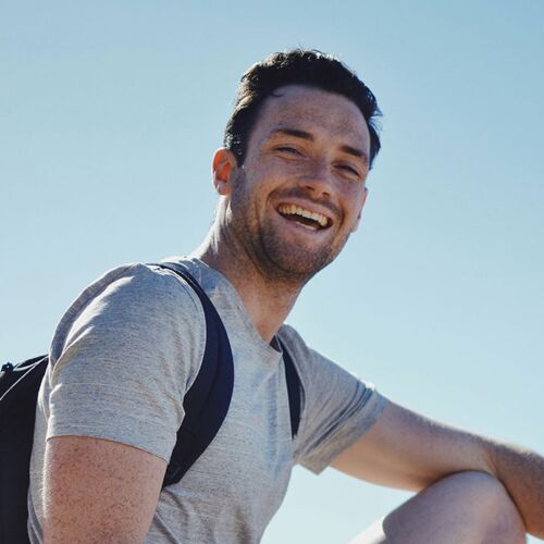 Junger Mann mit T-Shirt und mit Rucksack bei blauem Himmel